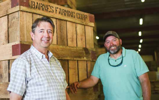 Two men posing in front of crate labeled Barnes Farming Corp